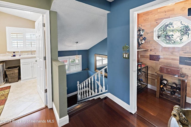 corridor featuring a textured ceiling, wooden walls, light hardwood / wood-style flooring, and vaulted ceiling