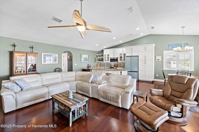 living room featuring ceiling fan with notable chandelier, dark hardwood / wood-style floors, a textured ceiling, and lofted ceiling