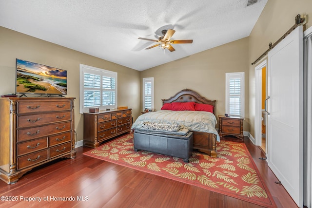 bedroom with vaulted ceiling, ceiling fan, dark hardwood / wood-style flooring, a barn door, and a textured ceiling