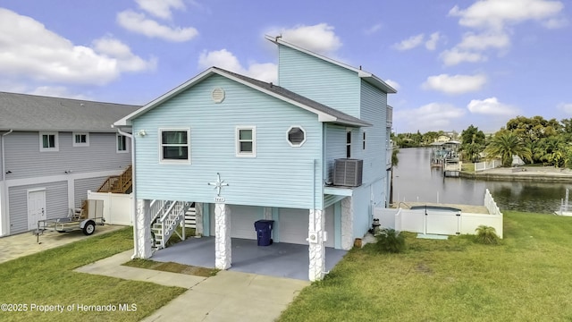 rear view of property featuring central AC unit, a garage, a water view, and a lawn