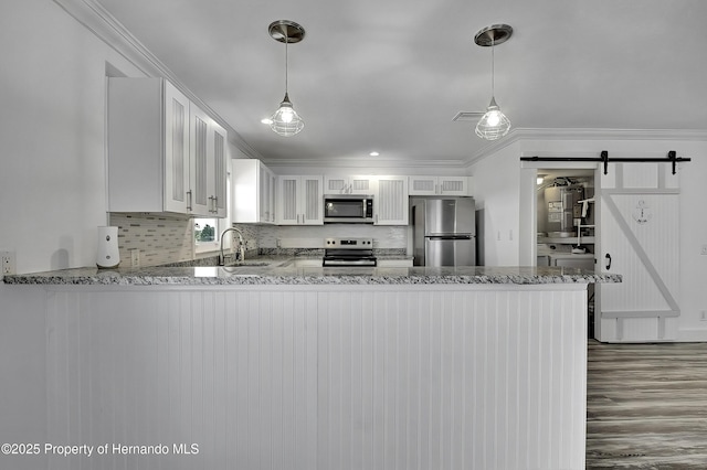 kitchen with a barn door, appliances with stainless steel finishes, kitchen peninsula, white cabinets, and tasteful backsplash