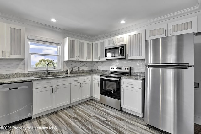 kitchen with stainless steel appliances, ornamental molding, light stone counters, white cabinets, and sink