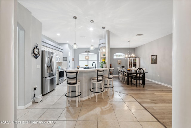 kitchen with hanging light fixtures, stainless steel appliances, light tile patterned floors, a kitchen bar, and a kitchen island