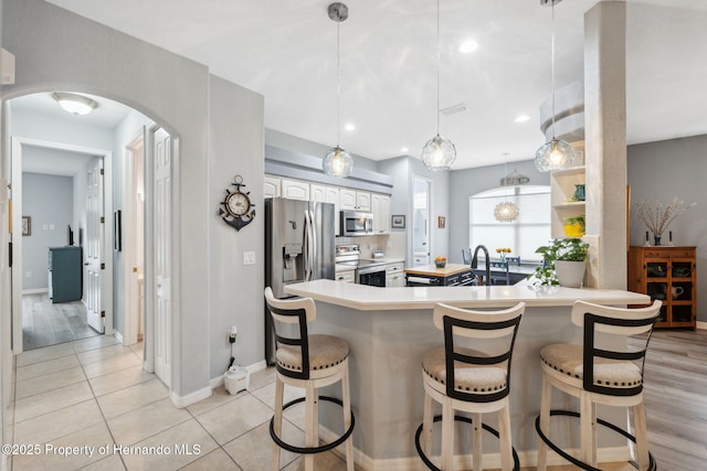 kitchen with stainless steel appliances, a kitchen bar, white cabinetry, decorative light fixtures, and light tile patterned flooring