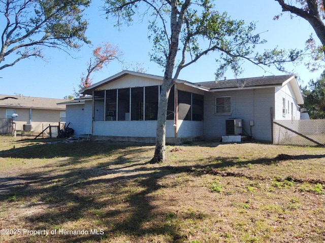 rear view of property with a lawn, central air condition unit, and a sunroom