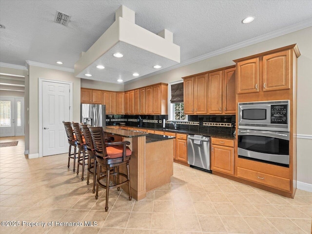 kitchen with stainless steel appliances, a kitchen breakfast bar, dark stone countertops, a kitchen island, and crown molding