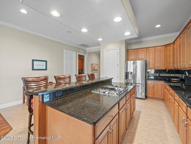 kitchen featuring a center island, a kitchen breakfast bar, ornamental molding, dark stone counters, and appliances with stainless steel finishes