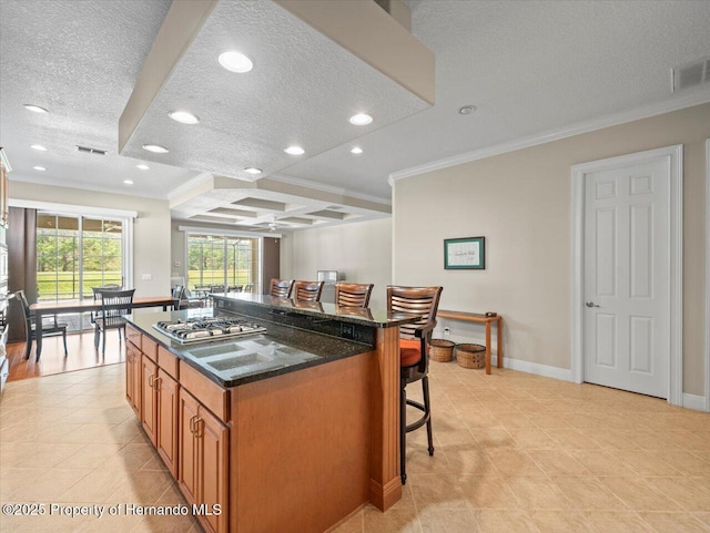 kitchen with a kitchen bar, dark stone countertops, ornamental molding, and a center island