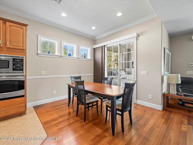 dining room with a textured ceiling, light hardwood / wood-style flooring, and ornamental molding