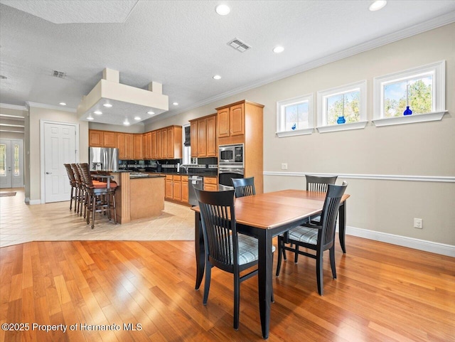 dining area with a textured ceiling, light wood-type flooring, and crown molding