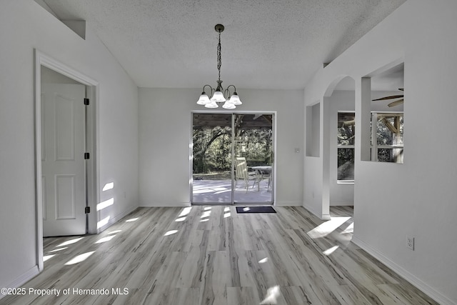 unfurnished dining area with a textured ceiling, light hardwood / wood-style flooring, and ceiling fan with notable chandelier