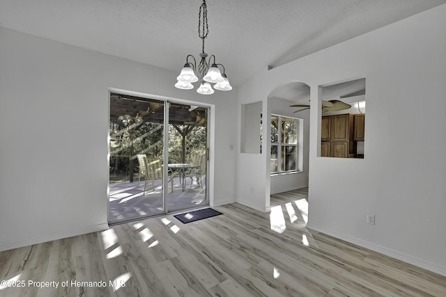 unfurnished dining area with ceiling fan with notable chandelier, a textured ceiling, light wood-type flooring, and vaulted ceiling