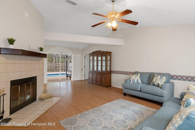 living room with light hardwood / wood-style floors, a tile fireplace, ceiling fan, and vaulted ceiling