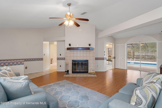 living room with ceiling fan, a tile fireplace, light hardwood / wood-style flooring, and lofted ceiling