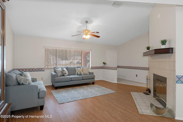 living room with ceiling fan, hardwood / wood-style floors, a tile fireplace, and vaulted ceiling