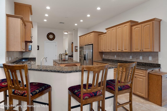 kitchen featuring a breakfast bar, backsplash, stainless steel appliances, and dark stone countertops