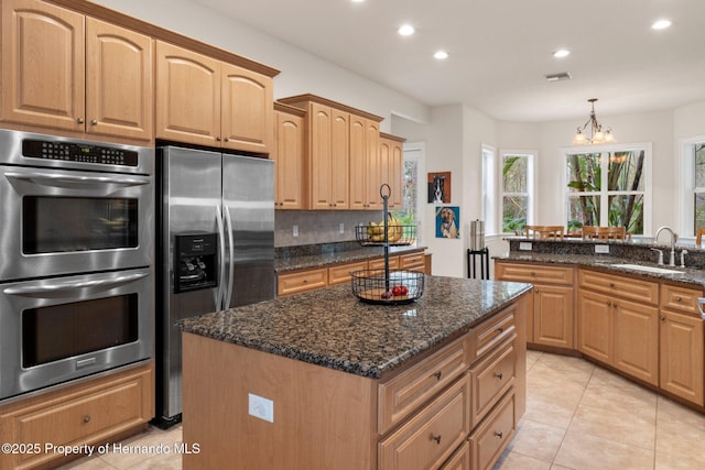 kitchen featuring appliances with stainless steel finishes, light tile patterned floors, sink, decorative light fixtures, and dark stone counters