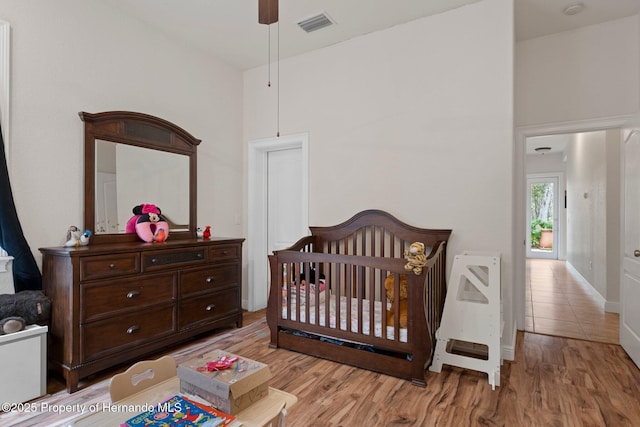 bedroom featuring a towering ceiling, light hardwood / wood-style floors, and a crib