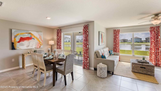 dining room featuring light tile patterned flooring, a textured ceiling, ceiling fan, and a water view