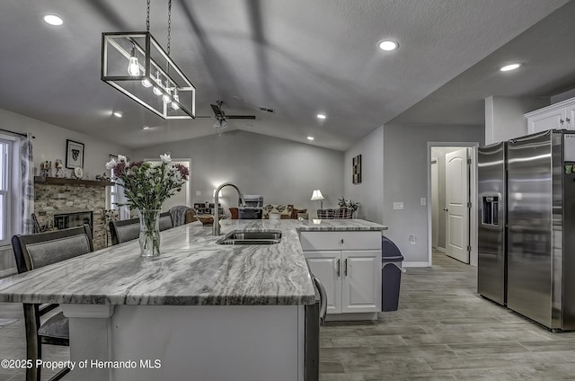 kitchen with sink, stainless steel fridge, white cabinetry, and lofted ceiling