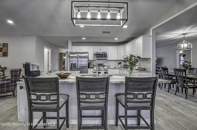 kitchen featuring white cabinets, tasteful backsplash, a breakfast bar area, hanging light fixtures, and appliances with stainless steel finishes