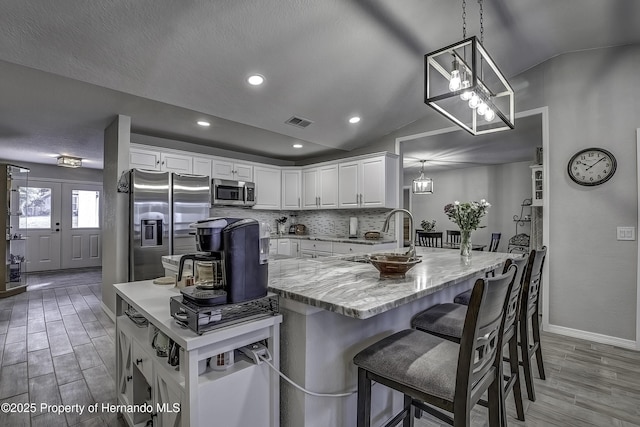 kitchen with decorative light fixtures, stainless steel appliances, lofted ceiling, white cabinetry, and sink