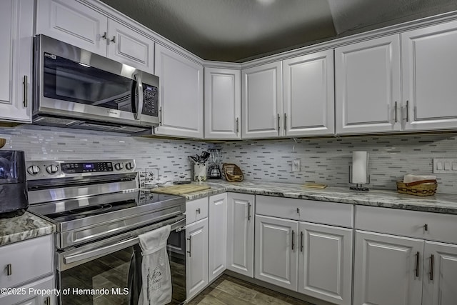 kitchen with stainless steel appliances, white cabinetry, light stone counters, and dark hardwood / wood-style floors