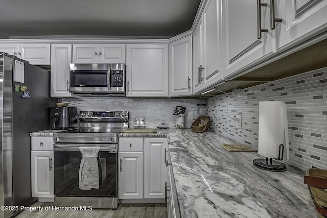 kitchen with light stone countertops, appliances with stainless steel finishes, tasteful backsplash, and white cabinetry