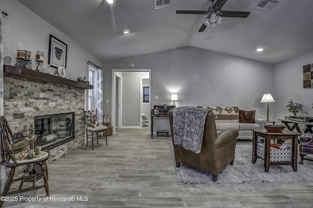 living room with ceiling fan, lofted ceiling, and a fireplace