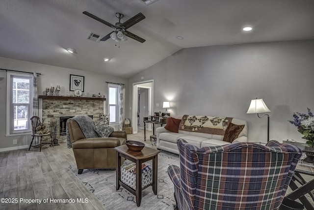 living room featuring a stone fireplace, light wood-type flooring, ceiling fan, and plenty of natural light