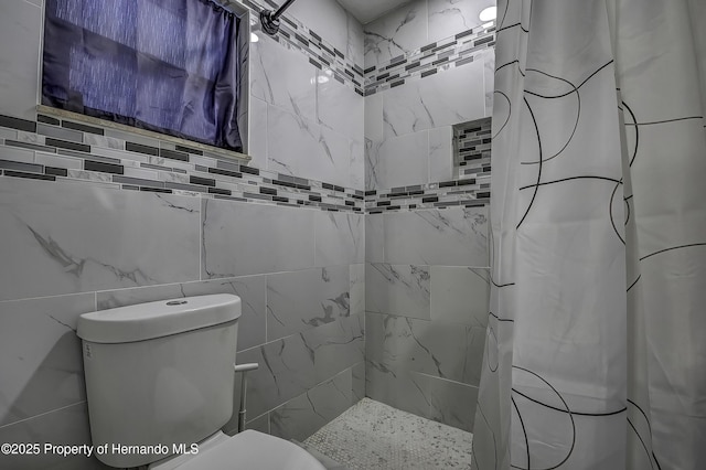 bathroom featuring toilet, curtained shower, and tile walls