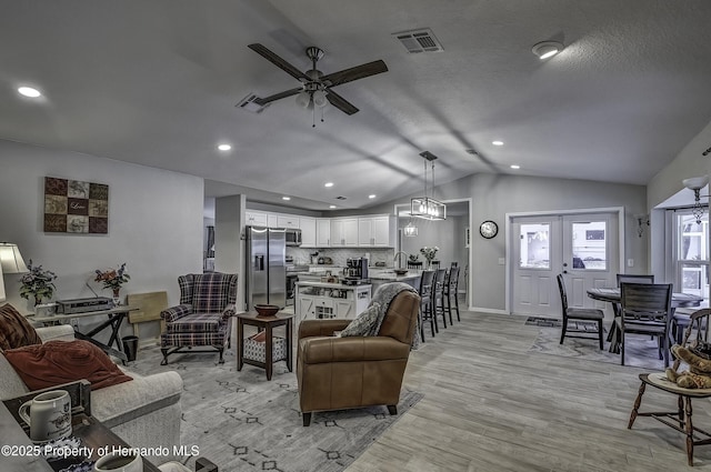 living room with vaulted ceiling, light wood-type flooring, ceiling fan, french doors, and a textured ceiling