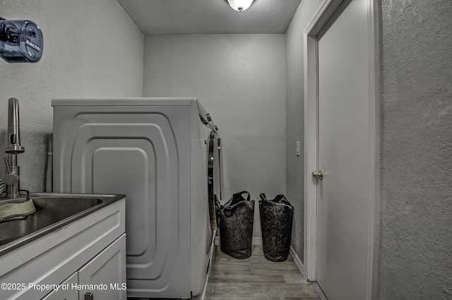 washroom featuring a textured ceiling, light hardwood / wood-style floors, and washer / clothes dryer