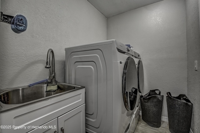 clothes washing area featuring sink, washing machine and clothes dryer, a textured ceiling, and cabinets