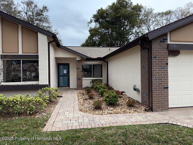 entrance to property with an attached garage, brick siding, and stucco siding