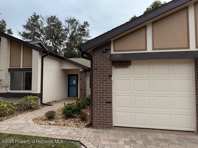 property entrance with an attached garage, stucco siding, decorative driveway, and brick siding