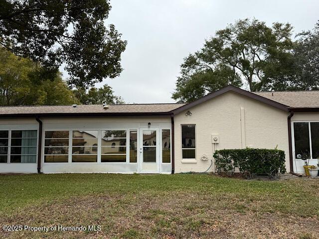 back of property featuring a lawn and stucco siding