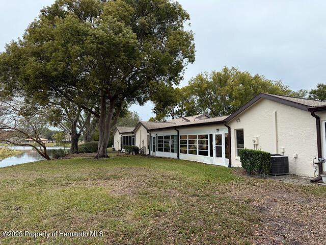 rear view of house with stucco siding, a yard, a water view, and central AC unit