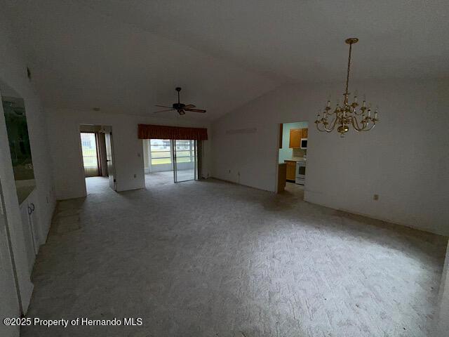 empty room featuring lofted ceiling and ceiling fan with notable chandelier