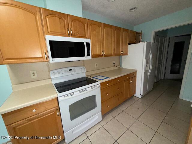 kitchen featuring brown cabinets, light countertops, light tile patterned flooring, a textured ceiling, and white appliances