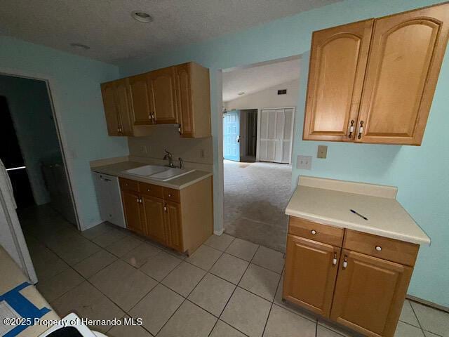 kitchen with light tile patterned floors, lofted ceiling, a sink, light countertops, and dishwasher