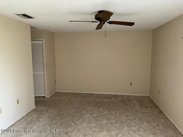 spare room with light carpet, visible vents, ceiling fan, and a textured ceiling