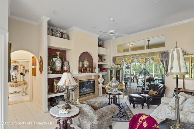 living room with light tile patterned floors, built in shelves, crown molding, a high end fireplace, and ceiling fan