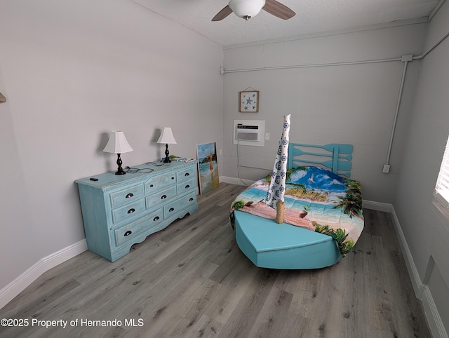 bedroom with ceiling fan, a textured ceiling, a wall mounted AC, and light wood-type flooring