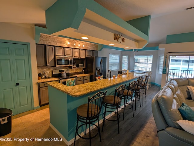 kitchen featuring a breakfast bar, backsplash, a kitchen island with sink, stainless steel appliances, and light stone countertops