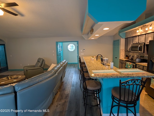 kitchen with a kitchen bar, hardwood / wood-style floors, an island with sink, appliances with stainless steel finishes, and backsplash