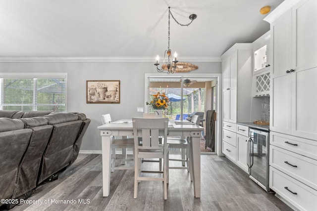 dining room with an inviting chandelier, dark hardwood / wood-style flooring, crown molding, and beverage cooler