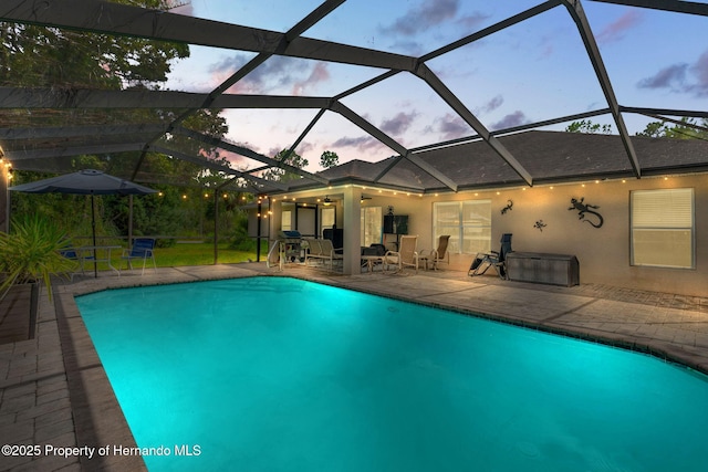 pool at dusk featuring ceiling fan, a patio area, and glass enclosure