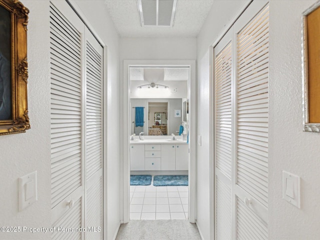 corridor with sink, a textured ceiling, and light tile patterned floors