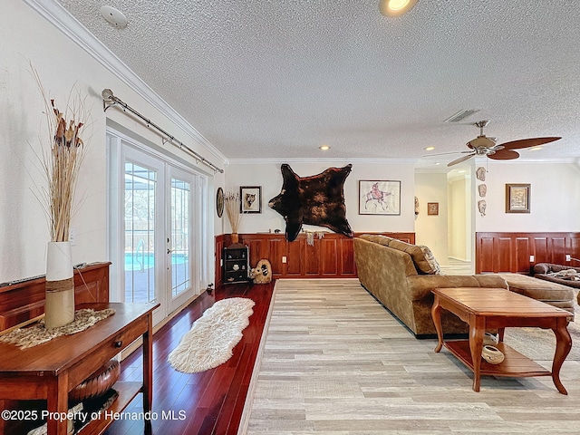 living room featuring ceiling fan, light hardwood / wood-style flooring, ornamental molding, a textured ceiling, and french doors